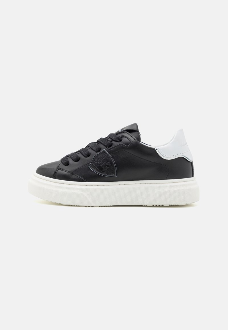 Baskets en cuir noir avec des accents blancs, bout rond, épaisse semelle en caoutchouc blanc, et lacets noirs. Comprend un détail de logo sur le côté.