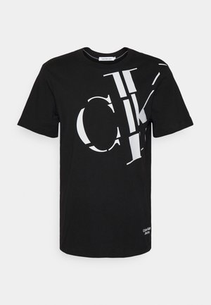 T-shirt noir à manches courtes avec un grand texte blanc fragmenté "Calvin Klein" sur le devant et un petit logo "Calvin Klein Jeans" près de l'ourlet.