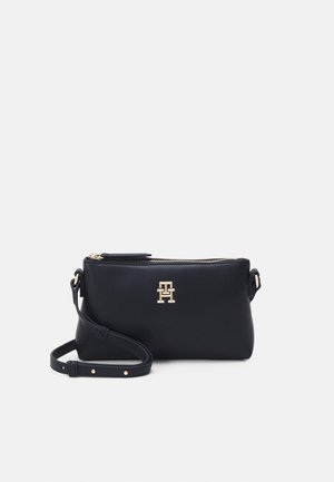 Kompakt sort lædertaske i crossbody-stil med gylden lynlås og justerbar rem, med et gyldent sammenlåst TH-logo foran.