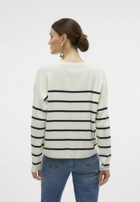Pull en crème à rayures avec des lignes horizontales navy, présentant une coupe décontractée et des manches longues, associé à un jean taille haute bleu.