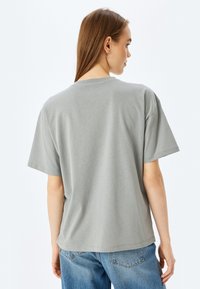 Camiseta de algodón gris con un corte relajado, mangas cortas y cuello redondo. Textura suave y diseño liso, con costuras en el dobladillo y las mangas.