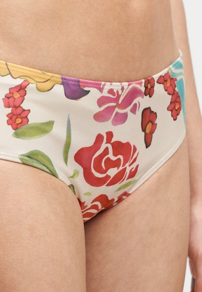 Gros plan d'une personne portant un bas de bikini à motifs floraux avec des fleurs rouges, roses, violettes et vertes sur un fond blanc.