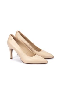 Tacones altos de cuero beige con diseño de punta puntiaguda, silueta estilizada y tacón de aguja de 3 pulgadas. Presentan un pequeño detalle dorado en el lateral.