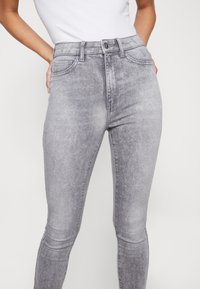 Jeans grises de cintura alta con una silueta ajustada, hechos de denim. Presentan bolsillos clásicos y un sutil desvanecimiento para aportar textura.