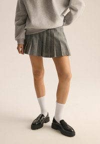 Szara spódnica w krate, plisowana, do kolan, zestawiona z białymi skarpetami i czarnymi masywnymi mokasynami. Miękka tekstura, strukturalny design oraz wzór w kratę.