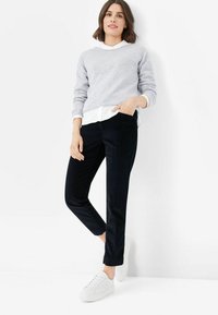 Grauer Pullover über einem weißen Kragenhemd, kombiniert mit navyblauen Cordhosen und weißen Sneakers. Schlichtes Design, weicher Stoff.