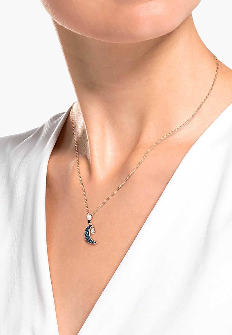Collar de cadena de oro con un colgante de media luna adornado con piedras preciosas azules y un pequeño acento de perla blanca. Textura suave y diseño elegante.