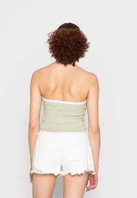 Um top cropped sem alças, em verde claro ribado com acabamentos brancos, combinado com calções de ganga brancos rasgados, apresentando um design ajustado e uma textura suave.
