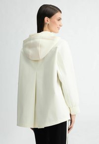 Lichtgele capuchonjack met een gladde textuur, oversized pasvorm en verlaagde schouders. Beschikt over zijsplitten en elastische manchetten.