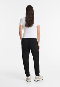 Black joggers with elastic waistband and cuffs, paired with a fitted white t-shirt. Casual footwear in light gray completes the outfit.