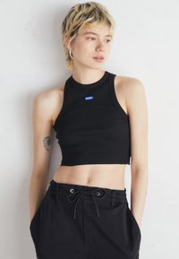 Black ribbed crop top with a round neckline, featuring a small blue "HUGO" logo. Worn with black drawstring shorts.