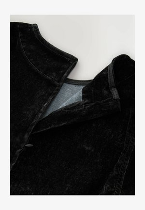 Primo piano del collo di un indumento in velluto nero con un rivestimento interno in tessuto grigio chiaro e una cerniera parzialmente aperta.