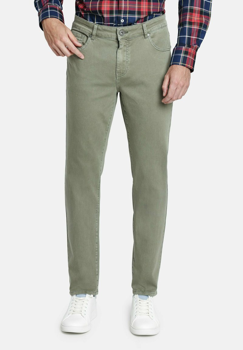 Pantalones de algodón verde claro con un corte clásico, que cuentan con bolsillos frontales, cremallera y perneras ligeramente ajustadas. Combinados con zapatillas blancas.