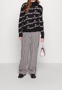 Černý pletený svetr s bílým vzorem "Láska"; kostkované černobílé kalhoty s širokými nohavicemi; růžová kabelka; černé boty.