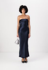 Αναίσθητο ναυτικό μπλε σατέν φόρεμα με εφαρμοστή σιλουέτα, μακριά μήκους και λεία υφή. Συνδυασμένο με ασημένια τσάντα και μαύρες γόβες.
