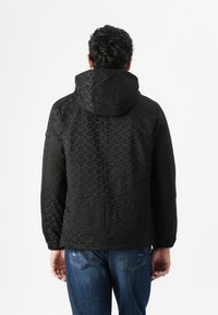 Chaqueta negra con capucha que presenta un patrón texturizado, puños elásticos y un corte relajado, combinada con jeans azules.