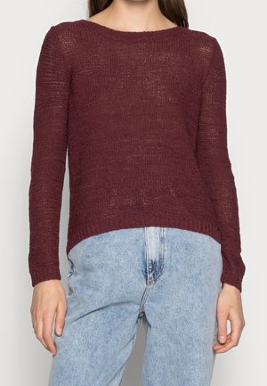 Pull en tricot bordeaux à manches longues, décolleté large, surface texturée et poignets côtelés, associé à un jean taille haute bleu clair.