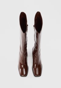 Botas de couro castanho e brilhante com biqueira quadrada, fecho de zipper e cano alto e afunilado. Textura suave, design elegante.