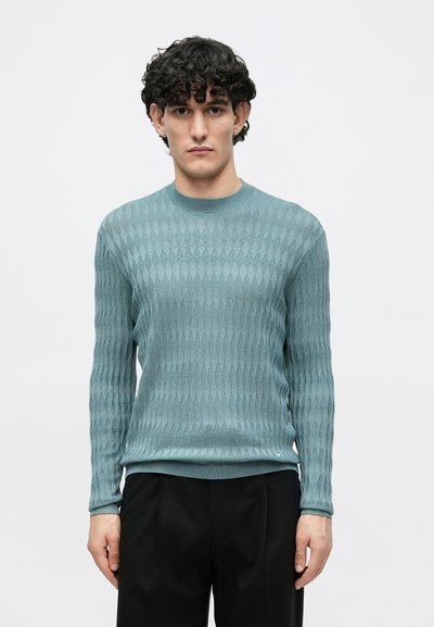 Ανοιχτό τιρκουάζ πουλόβερ με διαμάντι μοτίβο, ριμπ λαιμόκοψη και μανσέτες. Λεπτή υφή, μακριά μανίκια, σετάρισμένο με μαύρο παντελόνι.