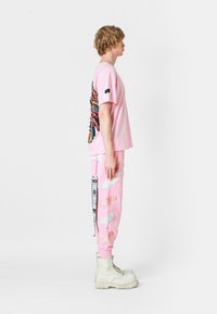 Camiseta de algodón rosa con un diseño colorido de mariposa en la espalda, combinada con pantalones de chándal rosas a juego que cuentan con alas blancas bordadas y parches.