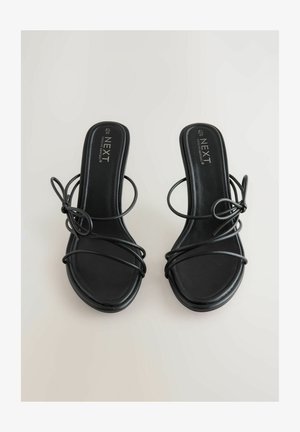 Svarta klacksandaler med flera tunna remmar, rundade tår och en slät matt yta. Logotyp prägla på fotbädden. Storlek 40.