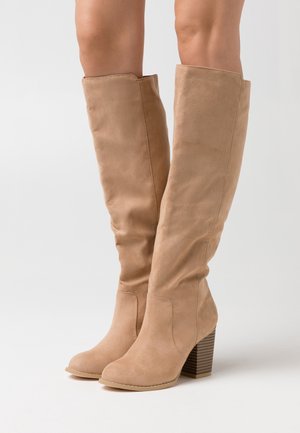 Botas de ante color tostado hasta la rodilla con una textura suave, punta redonda y un tacón en bloque a rayas. Diseño sencillo con acentos mínimos.