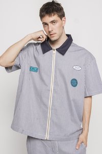 Oversized short-sleeve shirt in blue and white vertical stripes, featuring a navy collar, front zipper, and three patches.