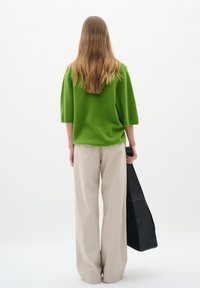 Green textured knit oversized sweater with short sleeves, paired with light beige wide-leg trousers, holding a black shoulder bag.