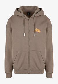 Sudadera con cremallera marrón, hecha de una tela suave, que cuenta con un bolsillo canguro, cordones ajustables y un diseño bordado en el pecho.