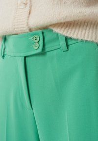 Pantalon vert menthe à la texture lisse, doté d'un devant plat, de deux boutons à la taille et d'une coupe ajustée avec des poches latérales.