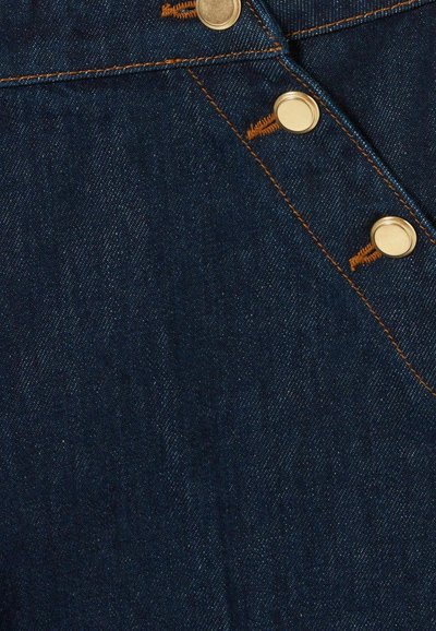 Tela de mezclilla en azul oscuro con trama diagonal visible, que presenta botones en tono dorado y detalles de costura en naranja contrastante a lo largo de las costuras.
