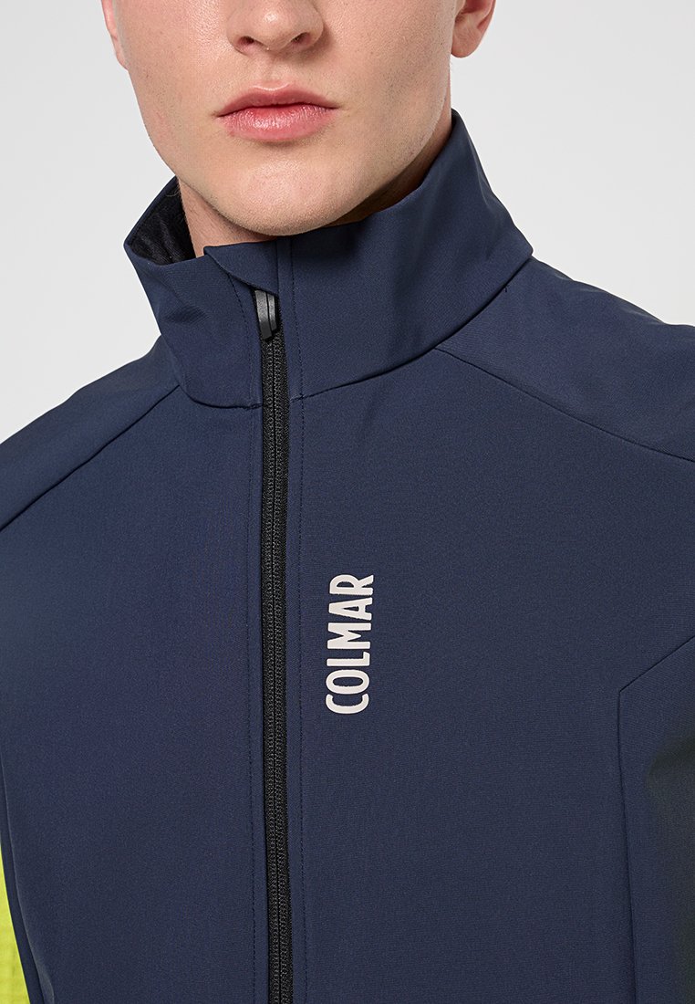 Giacca blu navy con colletto alto, zip frontale e logo. Il tessuto ha una superficie liscia e il design presenta cuciture delle spalle angolari.