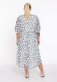 Witte jurk met een zwart en grijs gespikkeld patroon, doorschijnende stof, korte vlinder mouwen, elastische tailleband en een middellange rok.