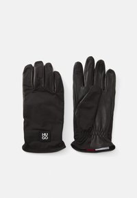 Gants noirs alliant cuir structuré et tissu lisse. Design de poignet froncé avec un petit écusson logo sur le poignet.