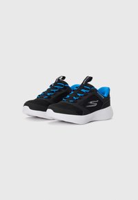 Et par svarte og blå Skechers slip-on sneakers med hvite såler, blå innermateriale og blå elastiske snører på hvit bakgrunn.