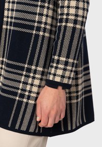 Mörkblå och gräddfärgad rutväv med en mjuk textur. Långärmad design med avslappnad passform och kontrasterande manschettdetalj.