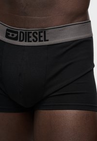 Homme portant un boxer Diesel noir avec une ceinture grise arborant le logo Diesel, vu de la taille à mi-cuisse.