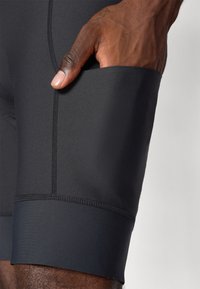 Talete scurte negre pentru sport, cu un design ajustat, fabricate dintr-un material neted și elastic. Caracteristici notabile includ un buzunar lateral și detalii de cusătură vizibile.