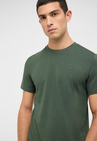 Ciemnozielona bawełniana koszulka z okrągłym dekoltem i krótkimi rękawami, z małym, haftowanym logo na piersi.