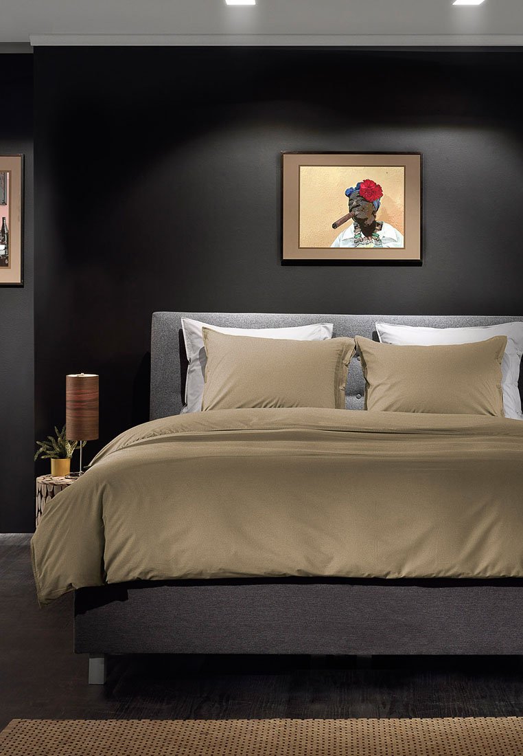 Bettwäsche-Set aus beigem Stoff mit zwei passenden Kissen auf einem dunklen, gepolsterten Bettgestell. Wandkunst in einem beigen Rahmen über dem Kopfteil.
