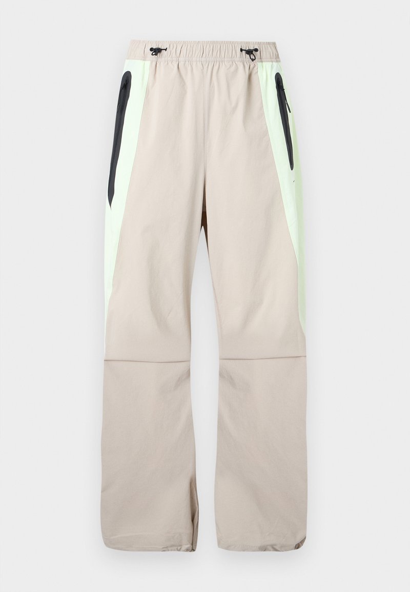 Beige broek met lichtgroene zijpanelen, zwarte dijzakken met rits en elastische tailleband met zwarte trekkoorden.