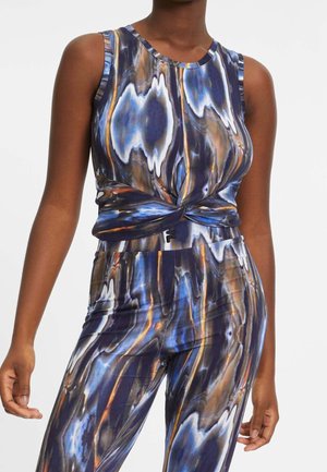 Mouwloos topje en broek met een blauw, zwart, wit en bruin abstract patroon, met een gedraaid detail aan de voorkant van het topje.