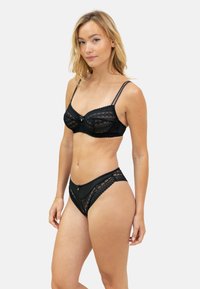 Ensemble de lingerie en dentelle noire comprenant un bralette avec des bretelles réglables, des motifs en maille décoratifs, et un bas de style bikini assorti avec des accents en dentelle.