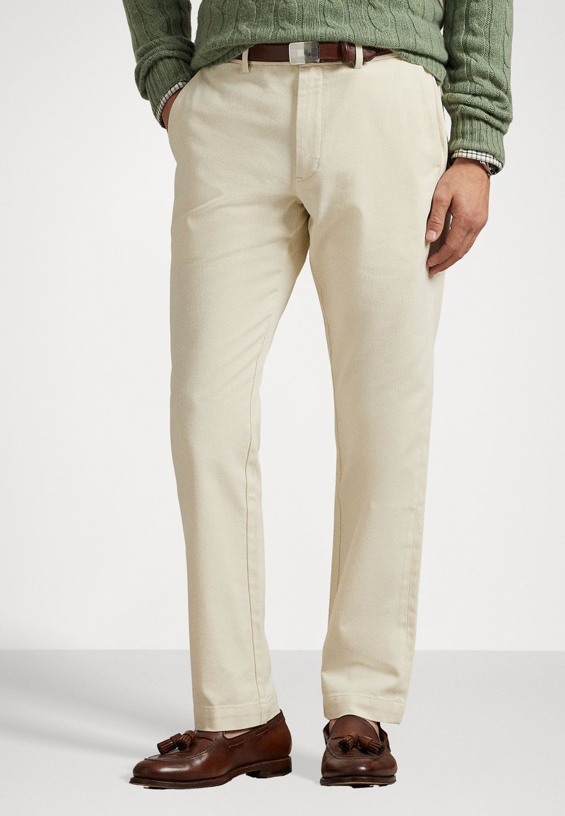 Μπεζ chinos φτιαγμένο από βαμβάκι με λεία υφή. Διαθέ�τει ίσια γραμμή, πλαϊνές τσέπες και καφέ δερμάτινη ζώνη με ασημένια αγκράφα.