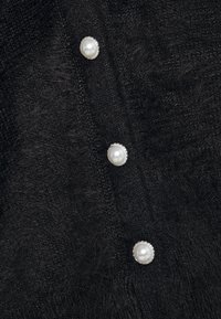 Tissu noir texturé avec une finition douce, comportant quatre boutons ronds brillants semblables à des perles, avec des accents de ton argenté.