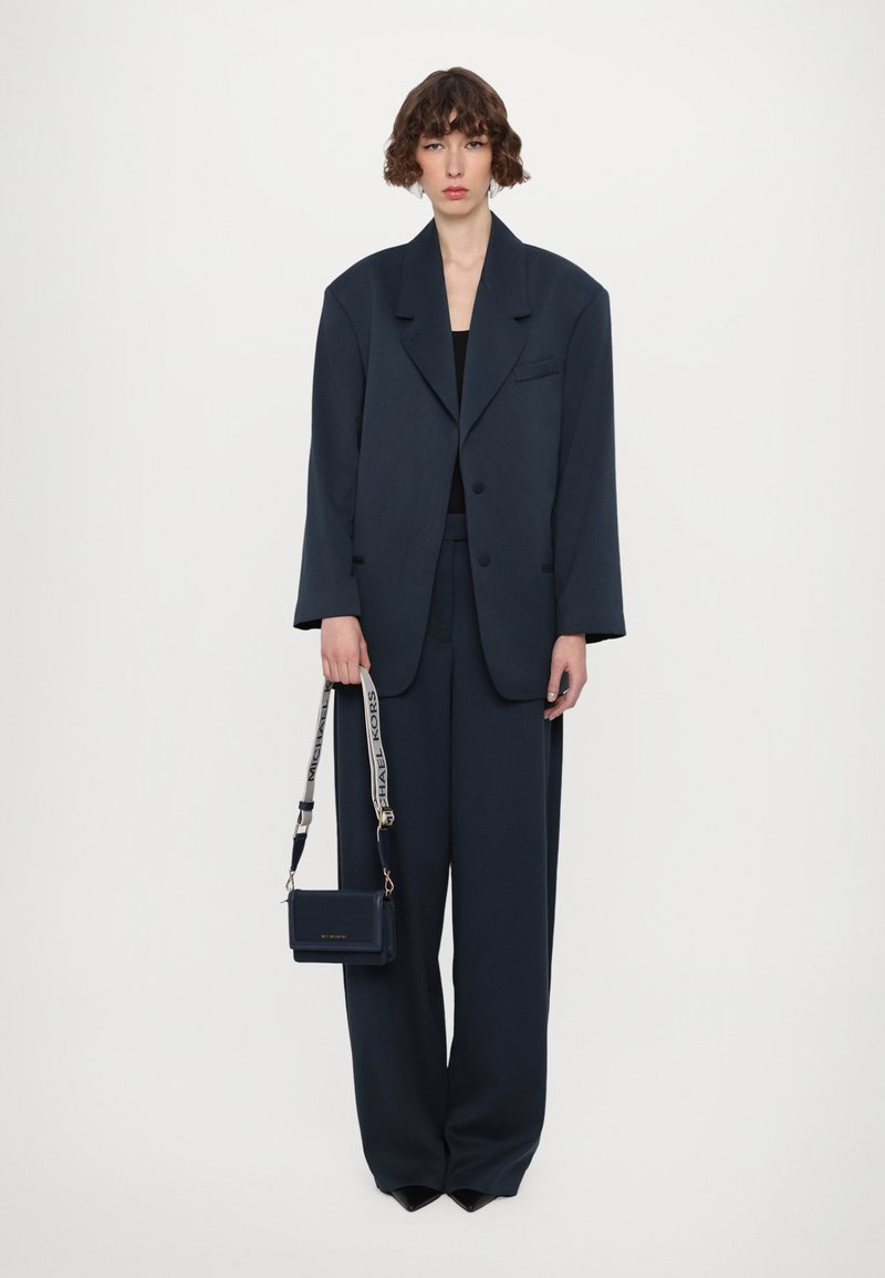 Mornarski oversize odijelo s strukturiranim blejzerom i hlačama širokih nogavica, u kombinaciji s malom torbicom preko tijela s remenom s logom.