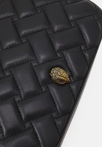 Clutch in pelle intrecciata nera con superficie texturizzata e un prominente dettaglio decorativo in bronzo che ricorda un occhio.