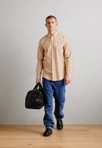 Chemise beige à boutons, jeans en denim bleu, chaussures en cuir noires et sac en cuir noir ; design minimaliste avec coupe régulière et sans motifs.