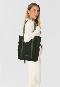 Zaino nero e verde con tessuto testurizzato, due tasche laterali e chiusure a fibbia. Presenta un design elegante e spallacci regolabili.