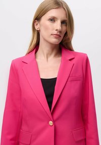 Fuksijasti blejzer sa strukturiranim dizajnom, reverima, jednim zlatnim dugmetom i malim bočnim džepom. Nosiv u kombinaciji s crnom majicom.